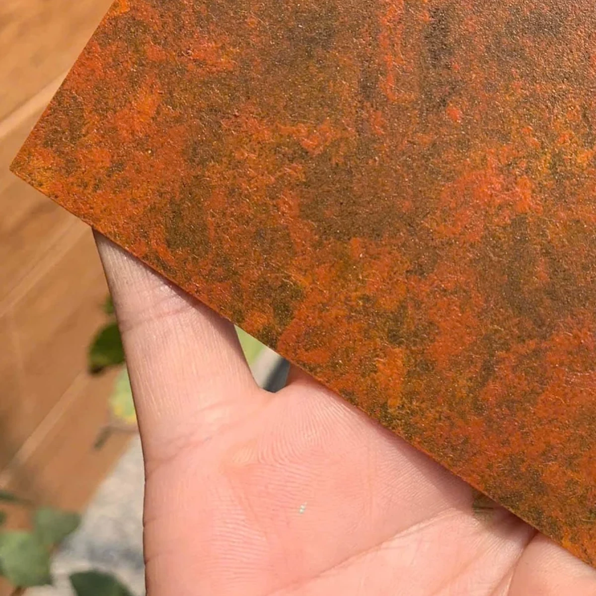 Cận bề mặt tấm mẫu phủ hiệu ứng giả rỉ sét trên lòng bàn tay, tông nâu ochre và cam đỏ