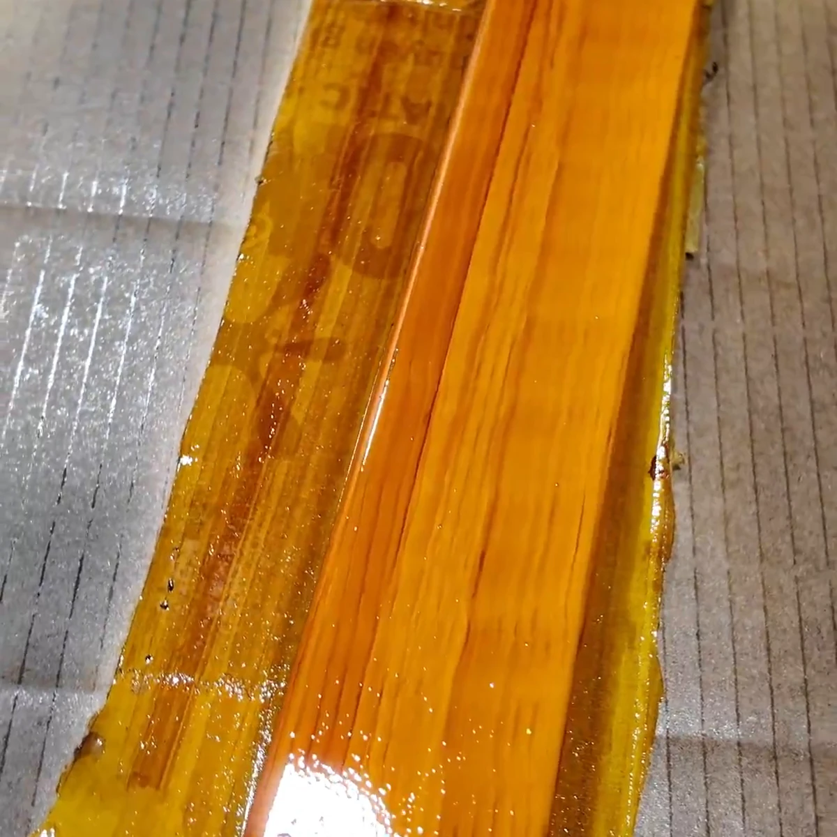 Mẫu thực vân gỗ trên thanh mẫu nền vàng nghệ đang thi công, với sắc vàng hổ phách và nét nâu đỏ mảnh