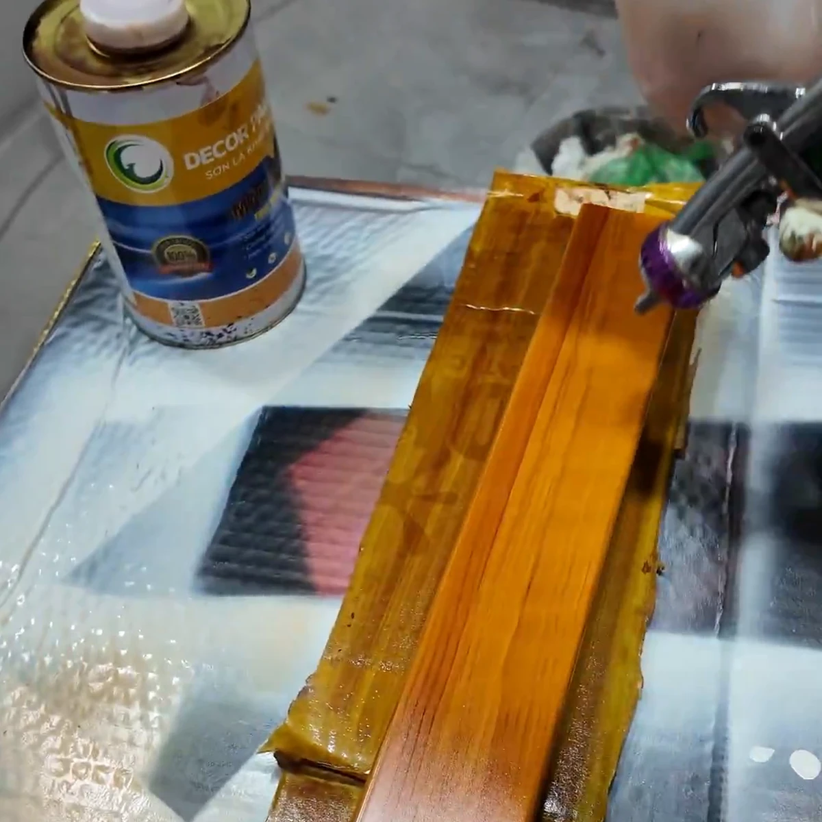 Thanh mẫu thực vân gỗ nền vàng nghệ đang được phun phủ, sắc vàng hổ phách và đường nâu mảnh